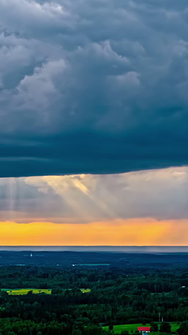 Vertical aerial time lapse of dramatic dark clouds breaking with golden sun rays beaming over rural Latvian countryside green fields forests meadows red house