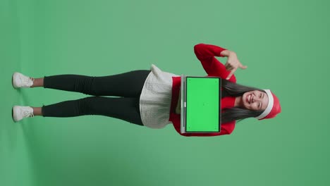 mujer con sombrero de santa sosteniendo una computadora portátil con pantalla verde