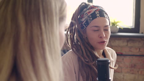 close up view of two women recording a podcast talking into a microphone sitting on sofa