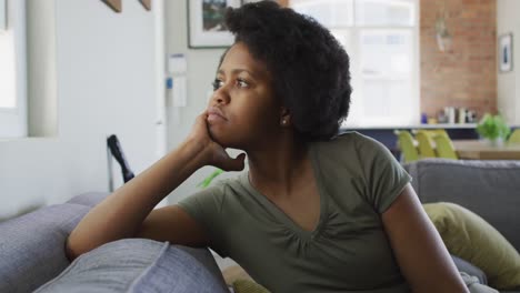thoughtful african american woman sitting on sofa, looking through window