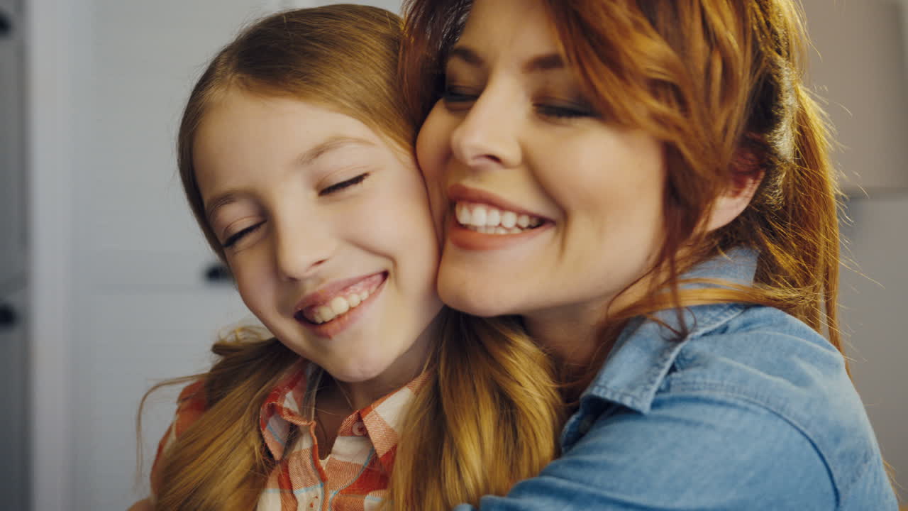 Portrait shot of the lovely pretty mother and daughter hugging and smiling in front of the camera and looking happy together. At home. Inside