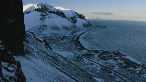 Birds-flying-around-rocky-cliffs-on-the-coast-of-snowy-Iceland---reverse,-drone-shot