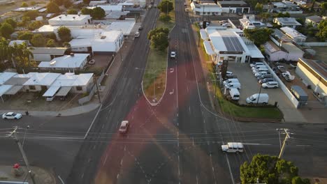 Drone-aerial-of-Mount-Isa-moving-backwards-panning-up-to-show-sun-flare-over-road-with-cars-driving