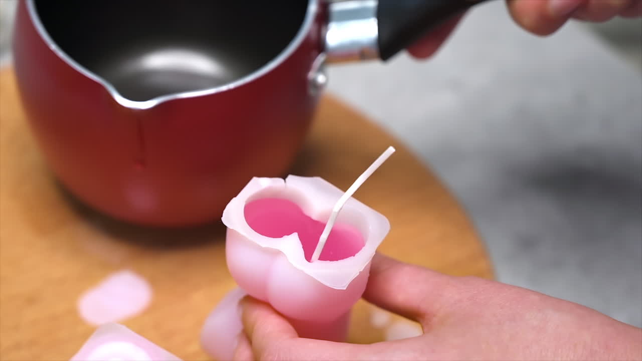 A woman occupied with hand made candles production, pouring melted wax into the mold. Slow motion