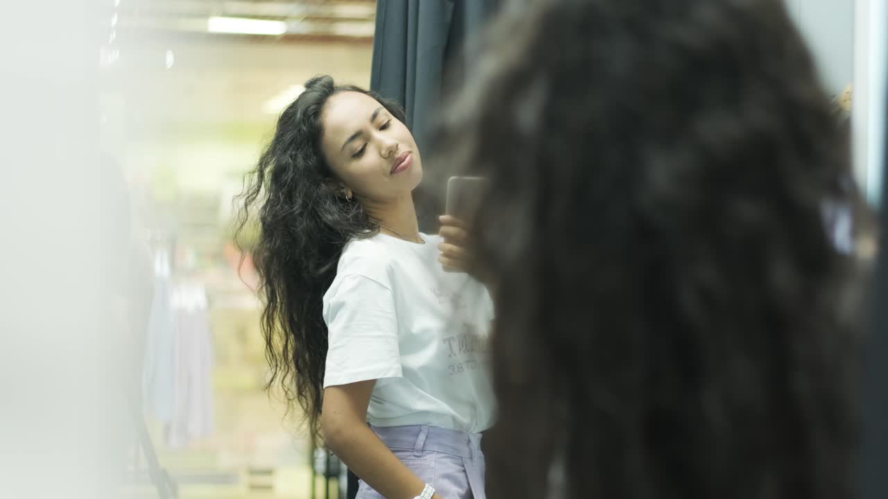 행복하고 세련된 소녀는 밝은 조명으로 인테리어 부티크 옷 가게의 드레싱 에서 옷을 시도합니다.