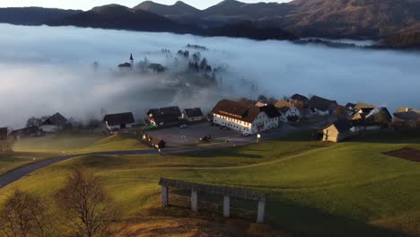 Drone-footage-of-an-alpine-village-in-the-morning-mist,-at-sunrise