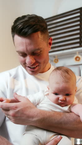 smiling caucasian mid-aged holding his newborn son. proud dad and his child at home. close up portrait. vertical video