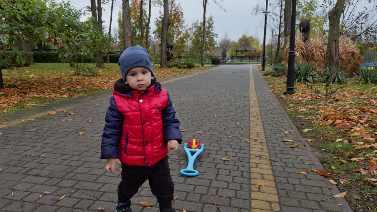 Following a cute boy wearing red jacket. Kid puts his toy on the ground and turns to camera.
