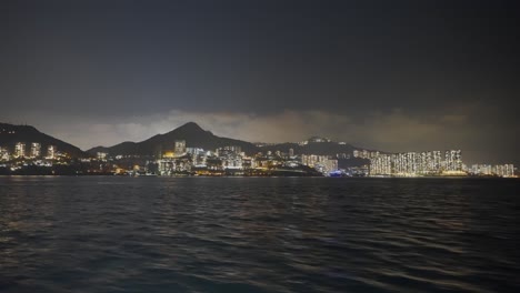 Aufnahme-Von-Einem-Boot-Aus,-Das-Mitten-In-Der-Nacht-Links-Von-Einer-Urbanisierten-Insel-Fährt