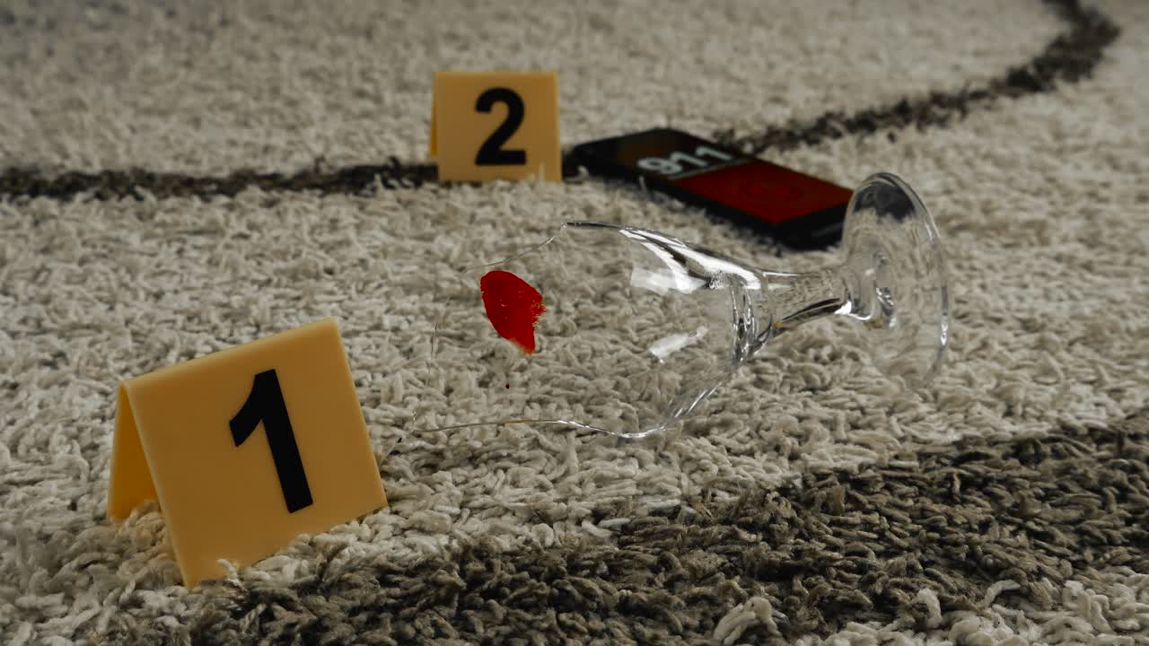 Close up view of a black gloved forensic police investigator hand placing a yellow crime scene marker next to a broken and bloody wine glass ona apartment carpet. Mobile phone in the back, 911 call