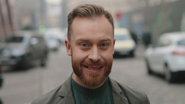Close-up view of caucasian businessman with beard turning his face to the camera and smiling joyfully in the street in autumn