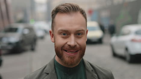 Close-up-view-of-caucasian-businessman-with-beard-turning-his-face-to-the-camera-and-smiling-joyfully-in-the-street-in-autumn