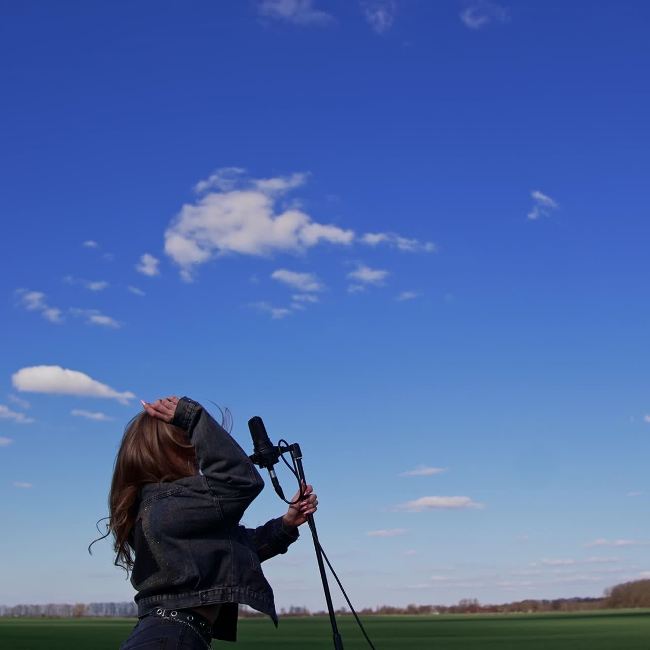 Beautiful young singer dancing with a microphone on a field. Pretty female soloist singing and jumping cheerfully outdoors. Slow motion