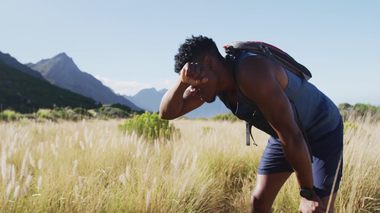 African american man cross country running resting wiping forehead in mountain countryside