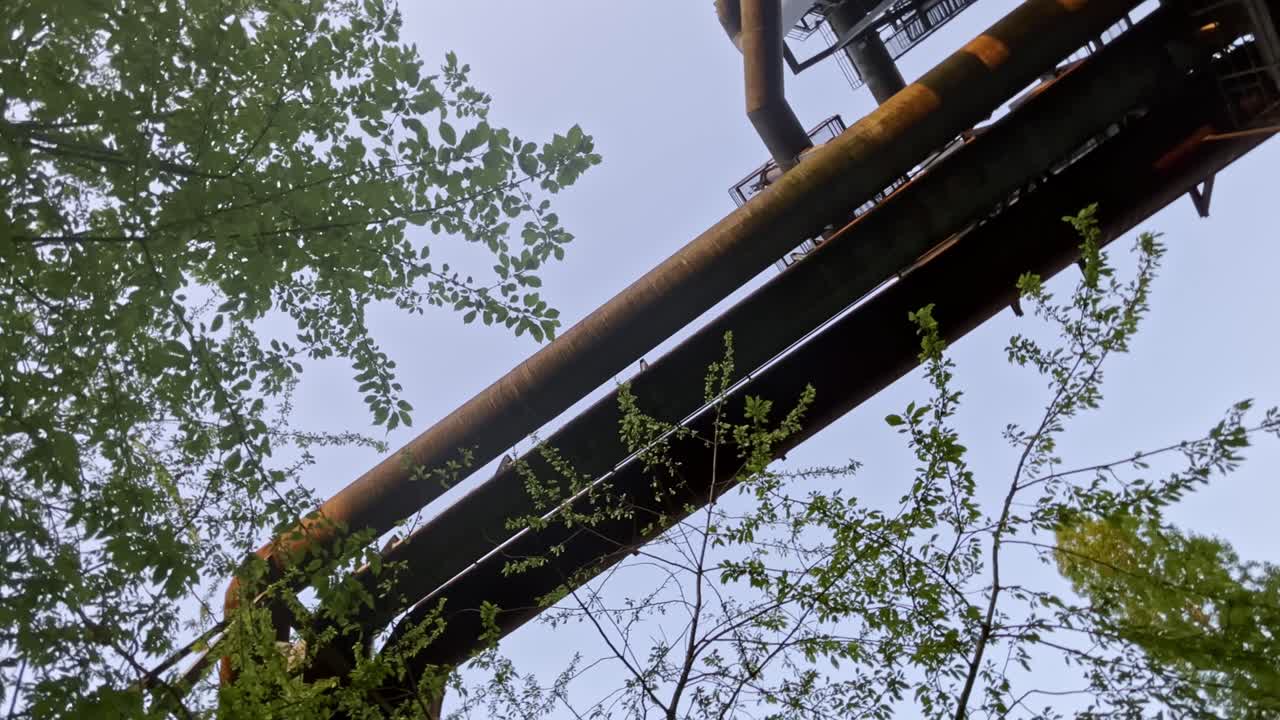 Tre store gamle rør på et stålværk omgivet af tæt natur under aftenhimmel i landskabsparken, Duisburg, Tyskland