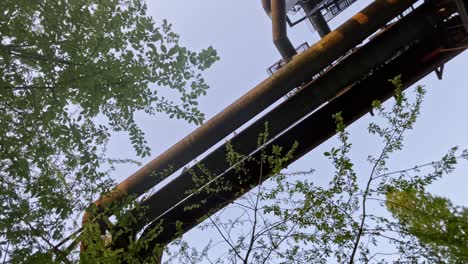 three-big-old-pipes-in-a-steel-mill-surrounded-by-dense-nature-at-evening-sky-in-landscape-park,-Duisburg,-Germany