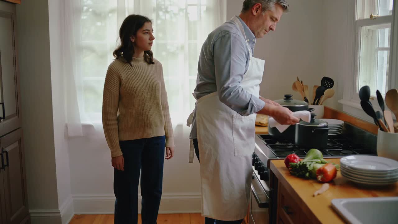 Homem de avental pegando uma toalha, limpando panelas, levantando tampas na cozinha de casa, preparando o jantar, menina observando