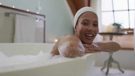 Portrait-of-mixed-race-woman-taking-a-bath-looking-at-camera-and-smiling