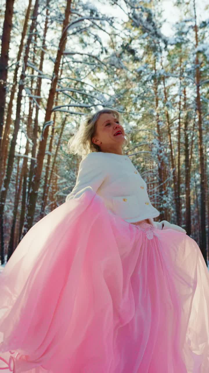 Donna gioiosa in gonna rosa che volteggia in una foresta invernale innevata.