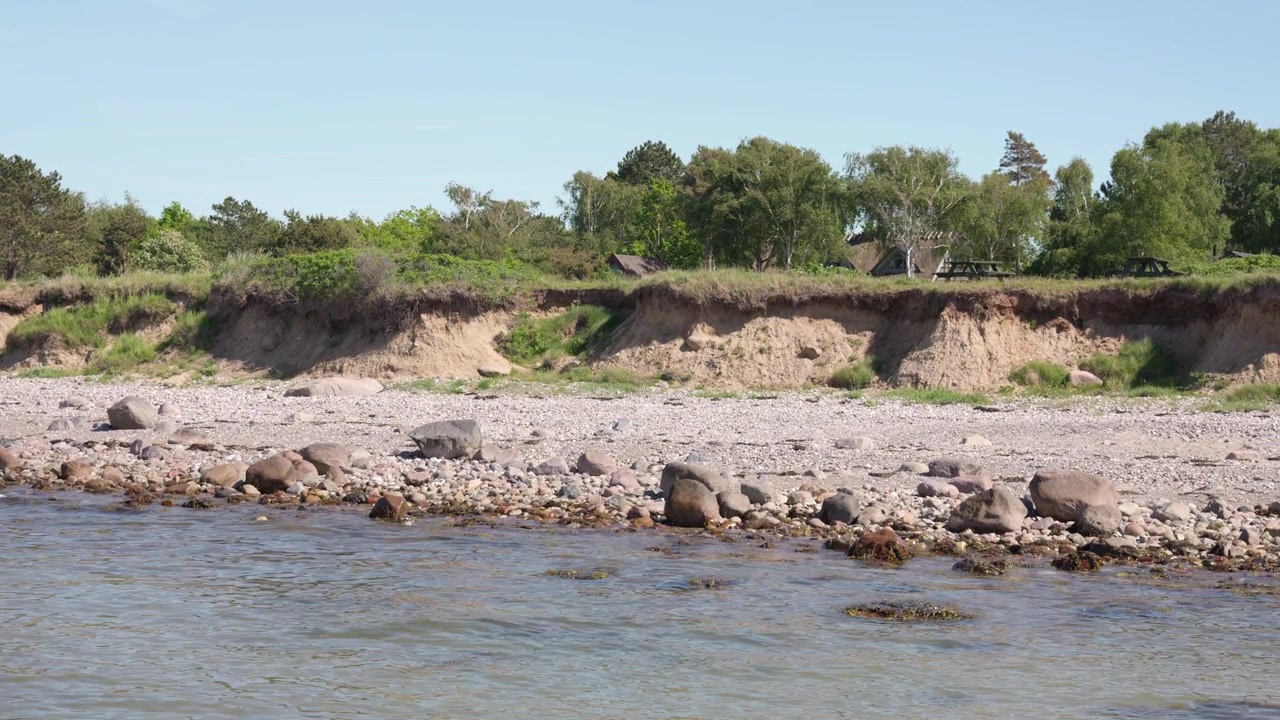 Rocky Shoreline with Waves and Lush Green Nature in Coastal Denmark
