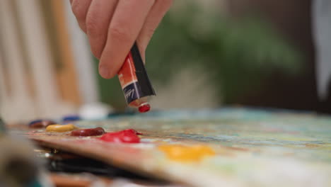 artist squeezes paint onto palette in studio closeup. artistic man prepares red acrylic pigment for drawing in shop. art teacher chooses color