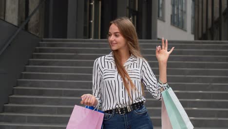 chica elegante sosteniendo bolsas de compras y mostrando el letrero ok. regocijándose con buenos descuentos de ventas de vacaciones