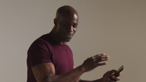 studio shot of excited mature man with mobile phone celebrating winning money against grey background 1