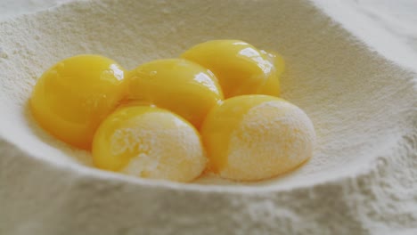 pouring egg yolks into well in flour pile on kitchen table