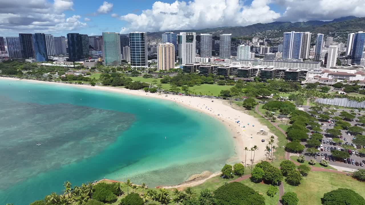 Aerial drone footage of tropical Waikiki Beach in Honolulu, Oahu, Hawaii, showing turquoise ocean waves, palm trees, and hotels along the coastline