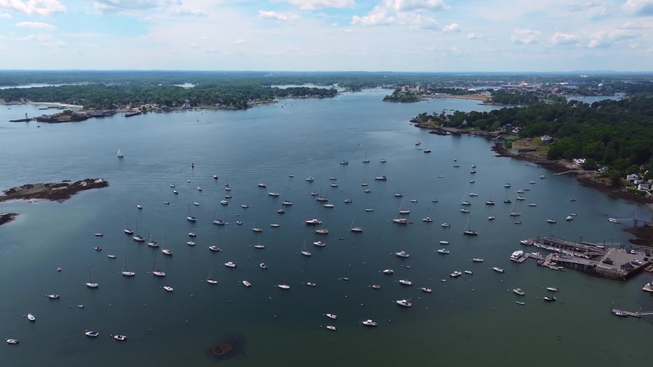 Ripresa aerea con drone dell'ampio fiume Piscataqua vicino a Kittery, nel Maine, con barche a vela sparse sull'acqua, coste rocciose e Portsmouth visibile in lontananza
