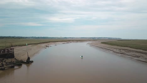 Man-kayaking-on-meandering-river,-drone-follows,-beautiful-landscape-in-the-background