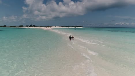 Paar-Mit-Kind-Auf-Dem-Arm-Läuft-Sandbank-Entlang,-Wellen-Spritzen-Nasse-Beine,-Von-Hinten