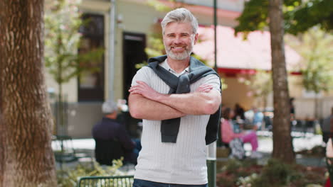 Portrait-of-happy-mature-man-stands-with-his-back-and-turns-around-smiling-friendly-arms-crossed