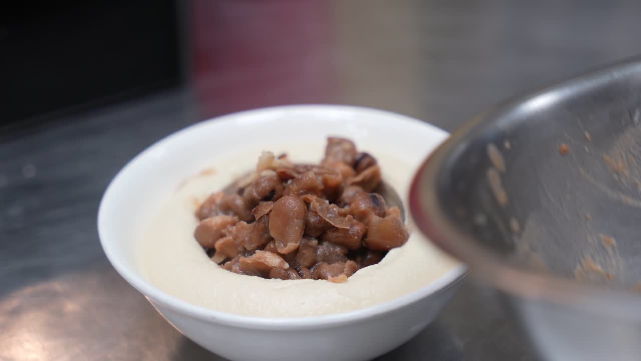 Close-up of spoon adding warm fava beans to creamy hummus, highlighting authentic Middle Eastern cuisine, perfect for cooking channels and food blogs