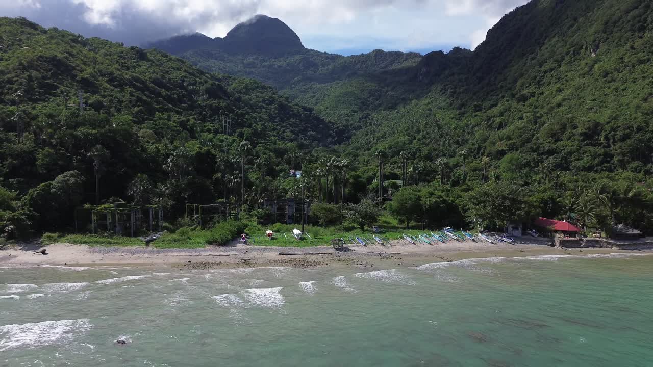 Vídeo aéreo con drones de barcos descansando en la playa Aninuan en Puerto Galera, Filipinas, con agua cristalina, playa de arena, bosque denso y montañas verdes al fondo, formando un paisaje tropical