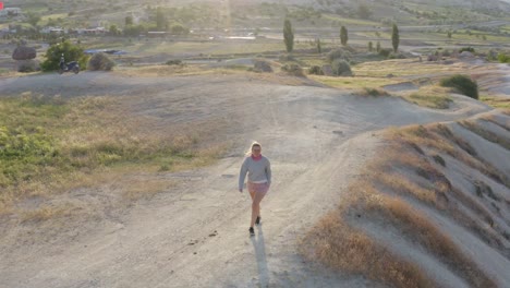 Blonde-female-in-pink-running-across-hill-in-Cappadocia-turkey-between-fairytale-chimney-formations-on-an-adventure