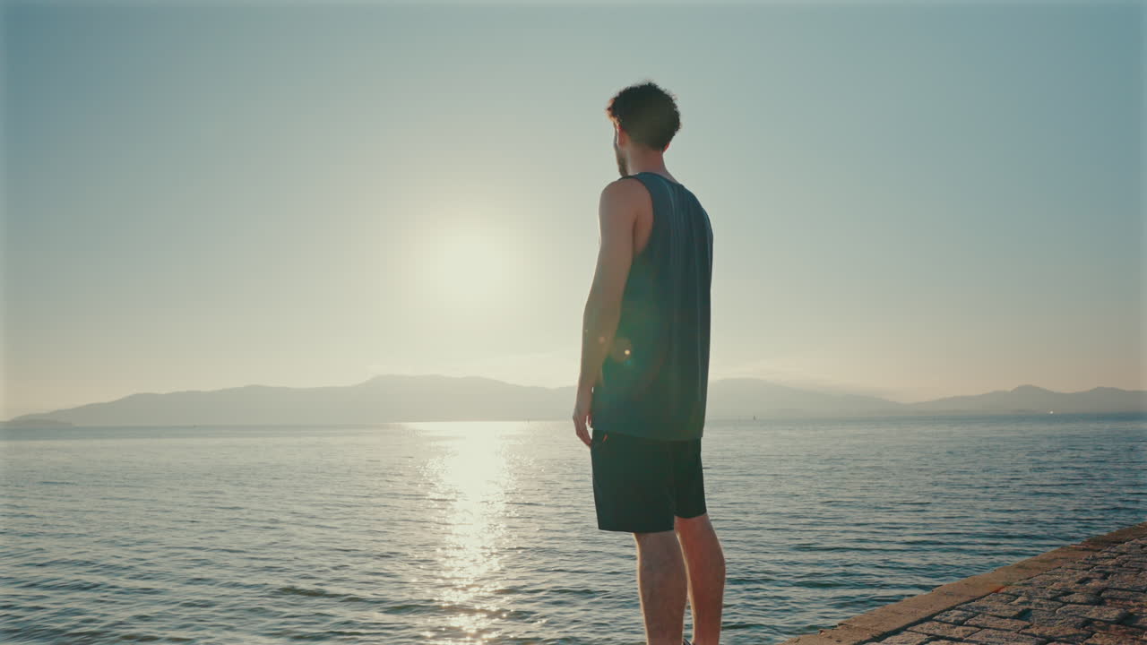 One man stands quietly on shallow water at sunrise, peacefully looking out over the calm sea