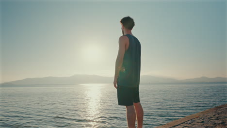 one man stands quietly on shallow water at sunrise, peacefully looking out over the calm sea