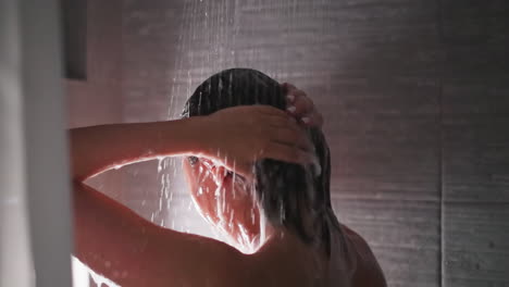 woman washes hair under shower sprays closeup. bare lady removes foam from head with water flow in bathroom. woman enjoys body washing at home