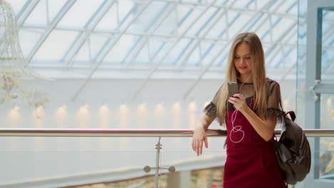 Portrait-of-cheerful-teen-girl-enjoying-music-in-stereo-accessory-connected-to-smartphone-entertaining-on-coffee-break,-smiling-woman-listening-radio-broadcast-via-app-on-cellular-sitting-in-cafe