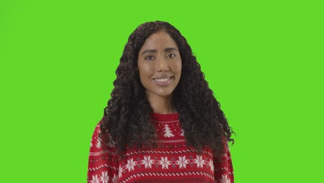 studio portrait of woman wearing christmas jumper against green screen smiling at camera