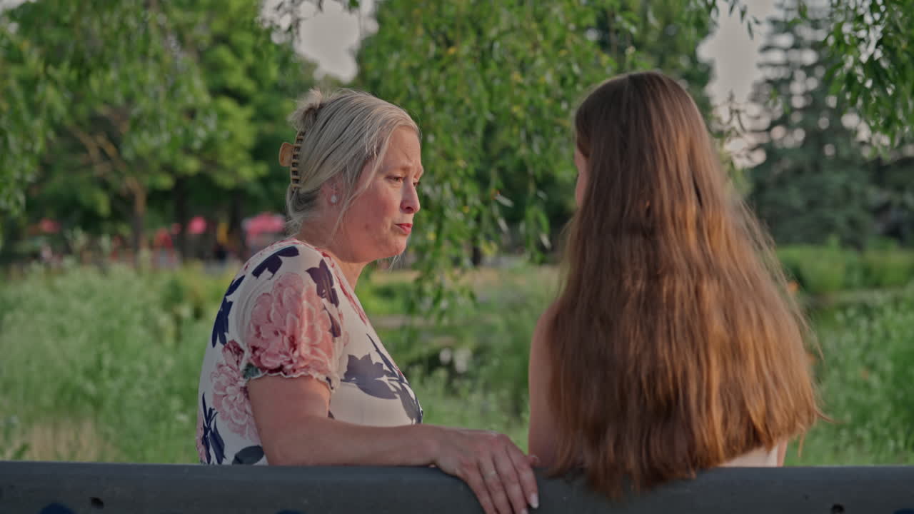 Emotional embrace between young woman and older mother figure after heartfelt conversation, in a vibrant public park during golden hour