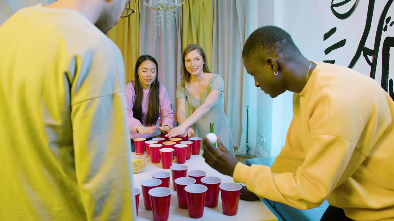 Happy multiethnic young friends playing beer pong at home