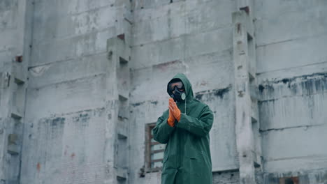 man in protective suit and mask in infected zone. person wearing respirator and safety uniform, in protective gloves standing on the background of abandoned building.