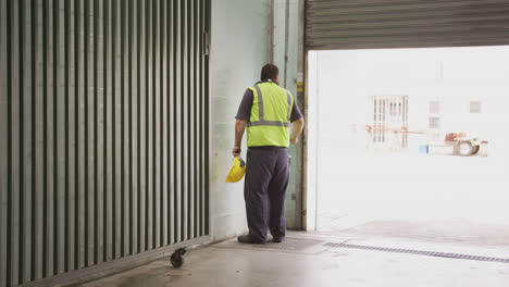 Trabajador-De-Fábrica-Caucásico-En-Una-Fábrica-Con-Un-Chaleco-De-Alta-Visibilidad,-Cerrando-Las-Puertas-Del-Almacén