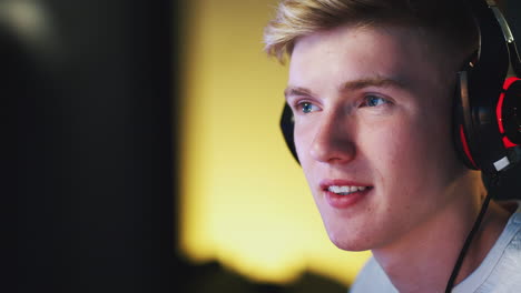 close up of teenage boy wearing headset gaming at home using dual computer screens