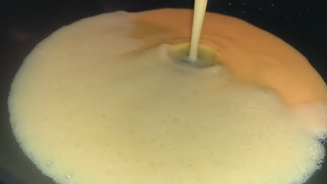 Slow-motion-shot-of-liquid-egg-mix-being-poured-down-a-frying-pan-to-make-an-omelet-or-thick-pancake