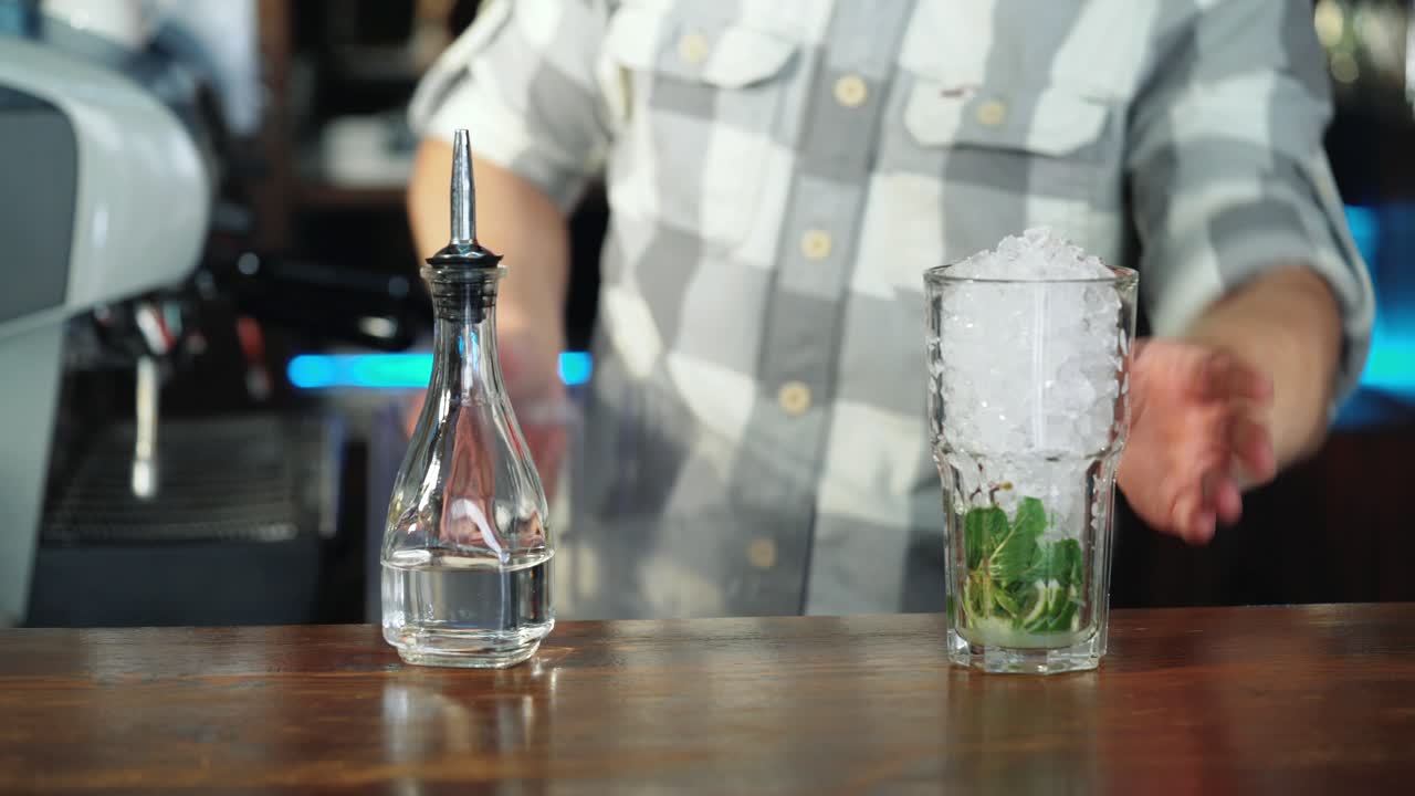 Barman adding an ice into the cocktail glass with a cane sugar and lime for making a delicious cocktail