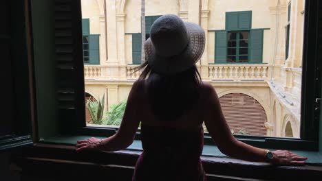 Girl-at-window-with-summer-hat-and-dress,-sunshine,-light-and-shadow