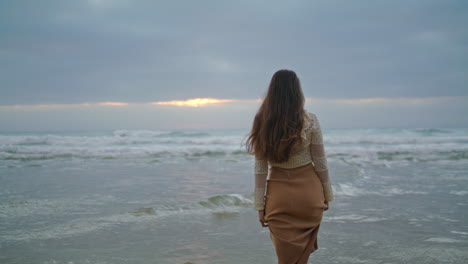 mujer soñadora caminando olas del océano de cerca. dama mirando vista al mar vertical de la noche